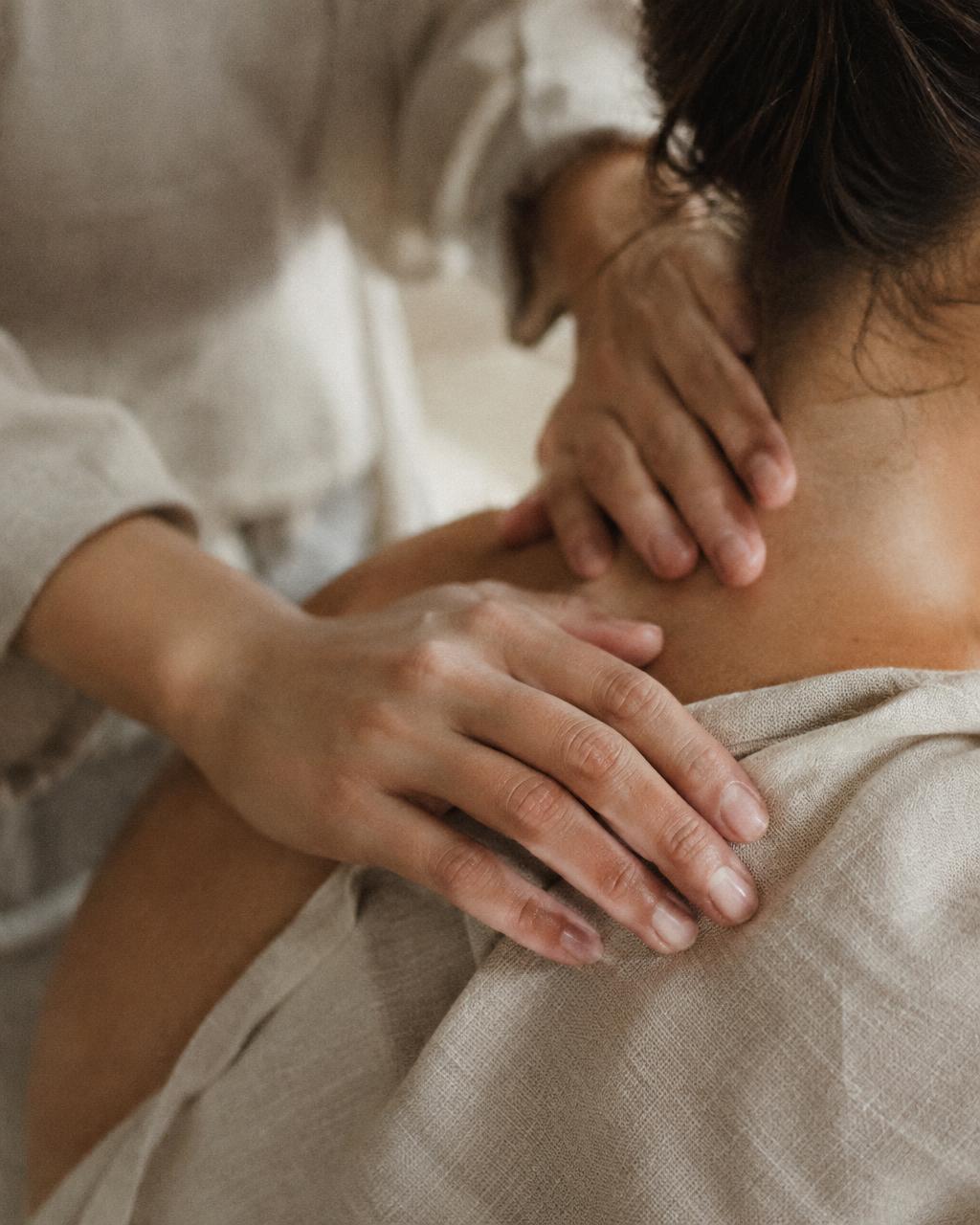 Practitioner's hands resting gently on a client's shoulder and neck over linen